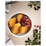 A bowl of plant-based, breaded, golden-brown nuggets with red sauce. Accompanied by green leaves and red berries.