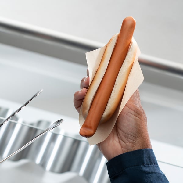 Ręka trzymająca hot doga z kurczakiem przy poręczy.