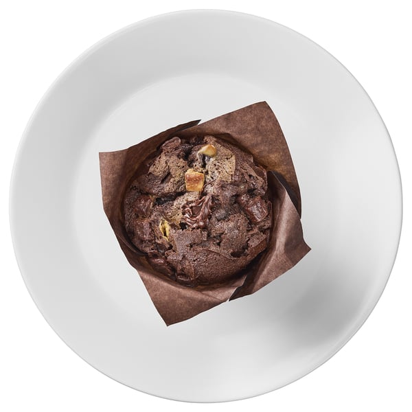 A chocolate muffin with dark, light, and white chocolate chunks sits in a tulip paper on a white plate.