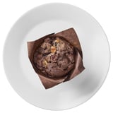 A chocolate muffin with dark, light, and white chocolate chunks sits in a tulip paper on a white plate.