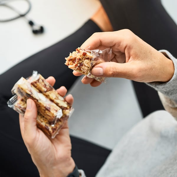 Hands holding cereal bars with nuts and honey, partly unwrapped.