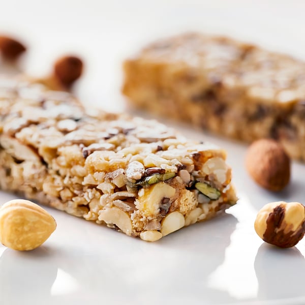 Nutty cereal bars with visible almonds, hazelnuts, and seeds on a white surface.