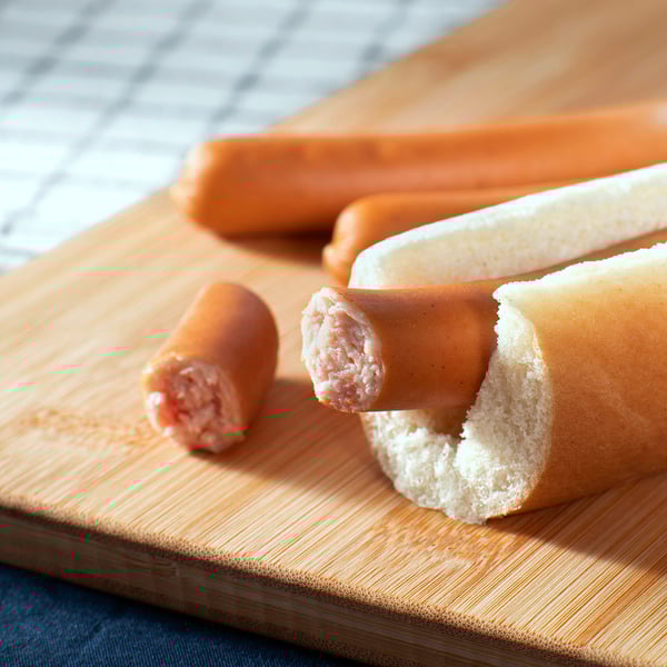 Wooden cutting board with three sausages. One cut open revealing filling, one inside bread.