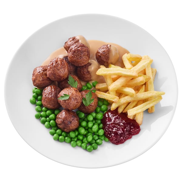 Assiette ronde blanche avec boulettes de viande, petits pois et frites.