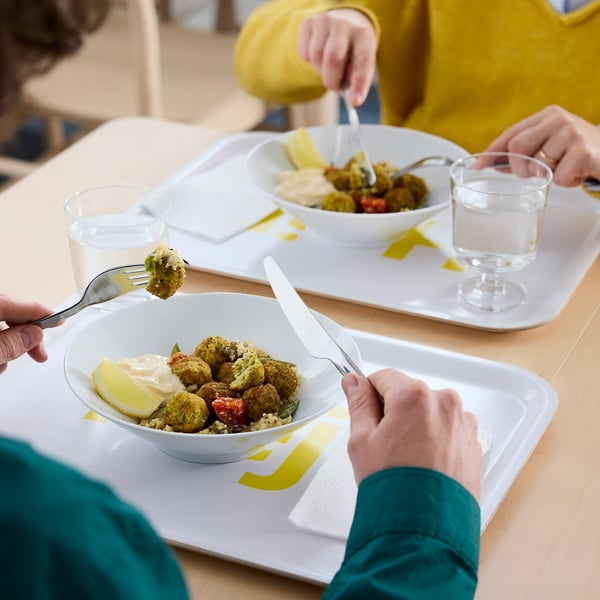 Two people eating healthy food: bowls with falafel, quinoa, and lemon in white trays.