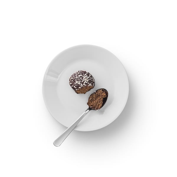 Una ciotola bianca contiene un dessert al cioccolato con scaglie di cocco; Su di esso poggia un cucchiaio.