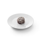 Piccolo tartufo tondo di cioccolato su piatto bianco con scaglie di cocco.