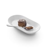 Piccolo dessert al cioccolato su piatto bianco con cucchiaio, guarnito con scaglie di cocco, rispecchia la semplicità moderna.