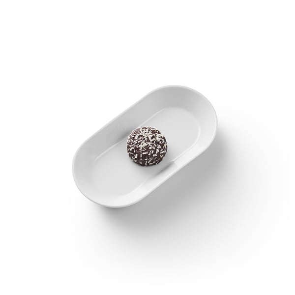 Un singolo dolcetto ricoperto di cioccolato con scaglie di cocco si trova su un piatto ovale bianco.