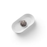 Un singolo dolcetto ricoperto di cioccolato con scaglie di cocco si trova su un piatto ovale bianco.