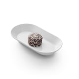 Un piccolo dessert rotondo ricoperto di cioccolato arrotolato in scaglie di cocco si trova in un piatto ovale bianco.