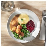 Assiette avec purée de pommes de terre, petits pois, boulettes de viande, sauce rouge. Fourchette et serviette sur le côté.