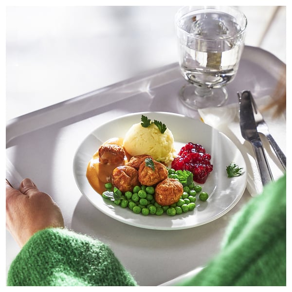 Un repas avec des boulettes de poulet, de la purée de pommes de terre, des pois et des canneberges sur une assiette blanche ; mangé avec un couteau et une fourchette.