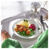 Un repas avec des boulettes de poulet, de la purée de pommes de terre, des pois et des canneberges sur une assiette blanche ; mangé avec un couteau et une fourchette.