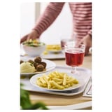 Ein Esstisch mit Tellern mit Essen und einem Glas rotem Getränk. Der Arm einer Person greift nach einer Schüssel.