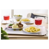 Teller mit Essen auf einem Tisch: Fleischbällchen, Kartoffelpüree, Pommes und Salat. Ein rotes Getränk wird in einem klaren Glas serviert.