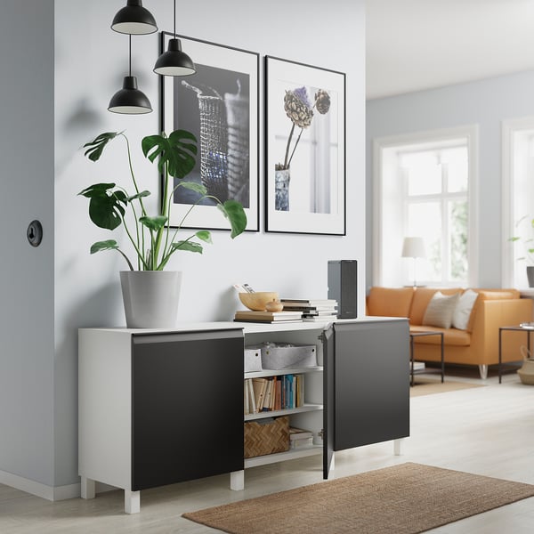 Nowoczesny salon z meblotą BESTÅ, rośliną, lampami, sztuką, pomarańczową sofą, dywanem, jasną przestrzenią.