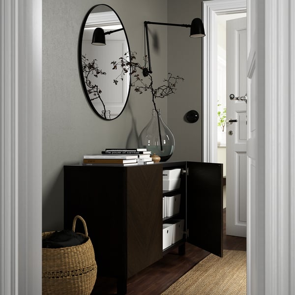 Nowoczesny salon z szafką z ciemnego drewna, otwartymi drzwiami, lustrem, odbiciem lampy, plecionym koszem.