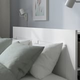 Nowoczesne łóżko z wysokim, minimalistycznym wezgłowiem, dwoma kinkietami i poduszkami, prezentujące jego oszczędzający miejsce design.