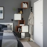 Nowoczesna sypialnia z półkami EKET, łącząca otwarte i zamknięte schowki, wysoko na ścianie. Szara pościel dopełnia minimalistyczny look.