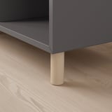 Szary schowek z drewnianymi nogami na jasnej drewnianej podłodze. Wysokiej jakości materiały i minimalistyczny design.