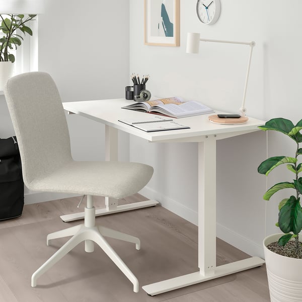 Krzesło biurowe ERFJÄLLET obok biurka z roślinami, lampą i książkami. Kompaktowa, elegancka konstrukcja.