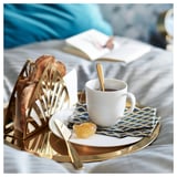 Mosiężna taca z chlebem, kawą, dżemem, nożem, łyżką na niebieskiej serwetce, białe łóżko.