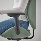Osoba siedząca na zielonym ergonomicznym krześle biurowym, pokazującym regulowane podłokietniki i tapicerowane siedzisko.
