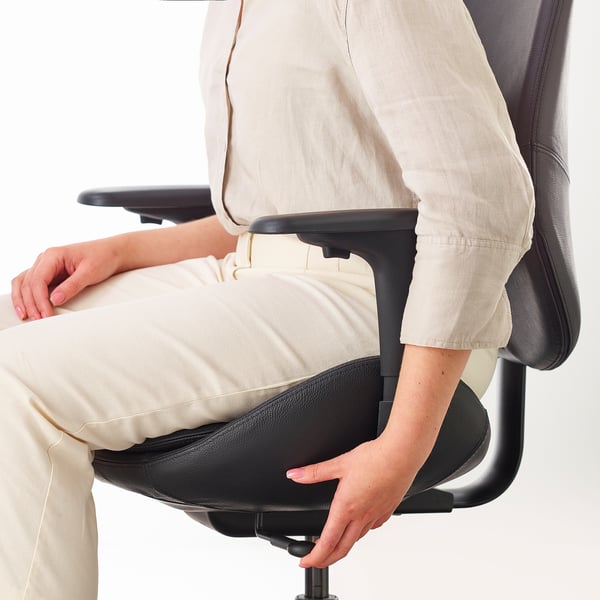 Osoba siedząca na ergonomicznym krześle biurowym z podparciem lędźwiowym i regulowanymi podłokietnikami.