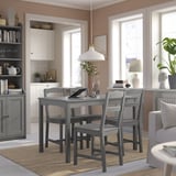 Nowoczesny szary zestaw jadalniany w salonie z drewnianym stołem i czterema pasującymi krzesłami. Biała lampa wisząca, naturalny wystrój i duże okna.