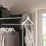 Nowoczesna szafa z szufladami z szarej tkaniny, białymi wieszakami, jasnoszarą sukienką i białymi ścianami. Na górze wisi torba i płaszcz.