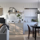 Nowoczesna przestrzeń dzienna ze ścianami w białe paski, szarą sofą, drewnianym stołem jadalnym i metalowym kredensem z drewnianymi szufladami.