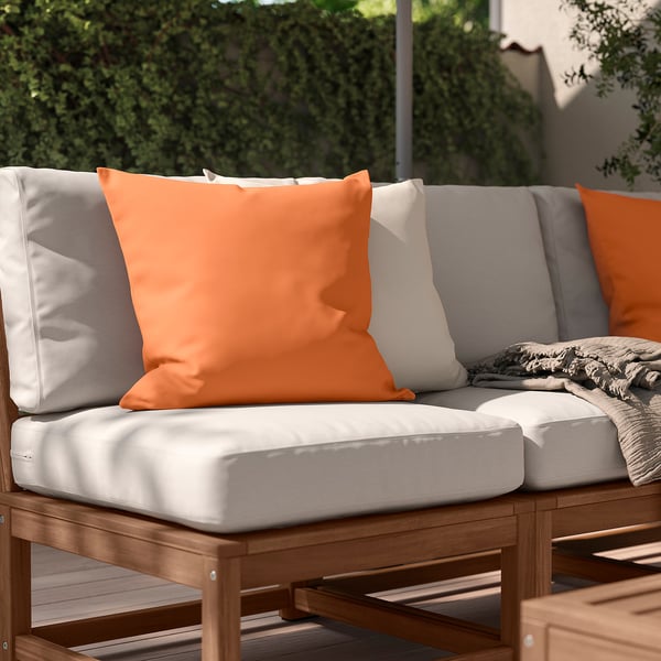 Zewnętrzna sofa segmentowa z pomarańczowymi, białymi poduszkami, drewnianą ramą, poduszkami.