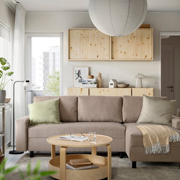 Nowoczesny salon z beżową sofą JÄRINGSHOLM, poduszkami, stolikiem kawowym i dużymi oknami.