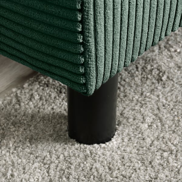 Nowoczesna sofa z zielonymi żebrami, solidnymi czarnymi nogami, na fakturowanym dywanie, prezentująca wysokiej jakości design i komfort.