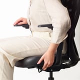 Osoba regulująca podparcie lędźwiowe na ergonomicznym krześle biurowym.