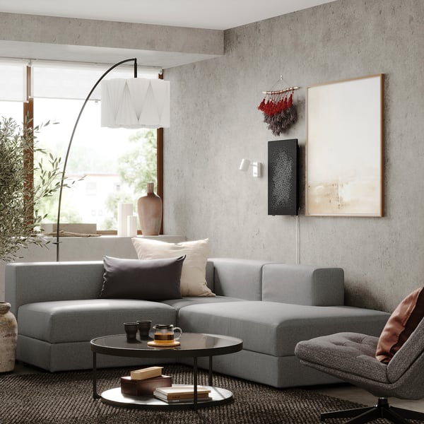 Nowoczesna sofa modułowa JÄTTEBO w salonie z poduszkami, okrągłym stolikiem kawowym, lampą podłogową i abstrakcyjną sztuką ścienną.
