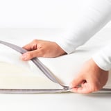 Zdjęcie przedstawia ręce zapinające materac do łóżeczka w celu łatwego czyszczenia.