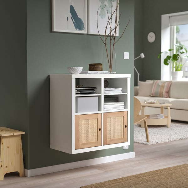 Nowoczesny salon z półką KALLAX, książkami, dekoracją, rośliną, sofą, stołem i zegarem.