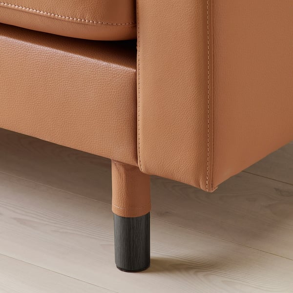 Zbliżenie na stylową, nowoczesną kanapę z jasnobrązowej skóry. Pokazuje szczegółowe szwy i solidną drewnianą nogę z czarną podstawą.
