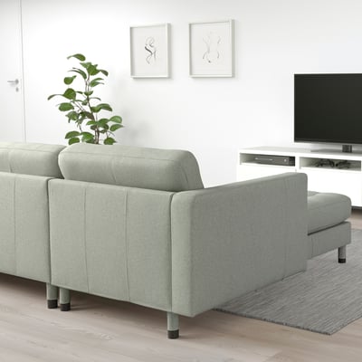 Nowoczesny, minimalistyczny salon z szarą sofą segmentową LANDSKRONA, eleganckimi drewnianymi nogami i stylową rośliną. Telewizor na stoisku naprzeciwko.
