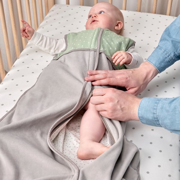 Dorosły zapina dziecko w przytulnym śpiworze w łóżeczku. Zapewnia bezpieczny, komfortowy sen.