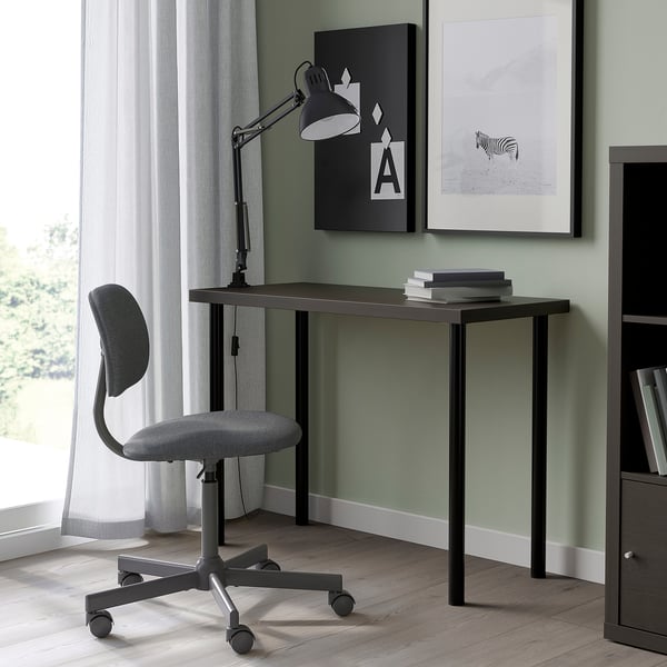 Minimalistyczne domowe biuro: czarne biurko LINNMON, szare krzesło, zielona ściana, lampa, książki, sztuka.