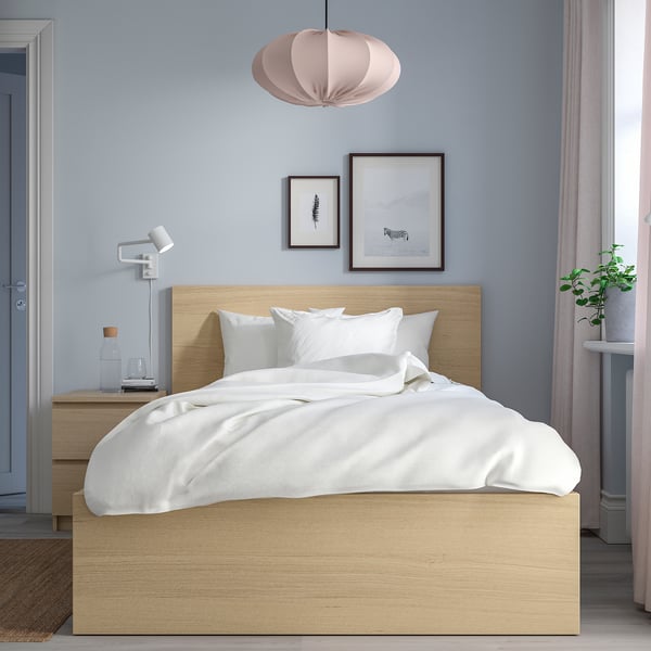 Przytulna sypialnia z łóżkiem MALM, białą pościelą, niebieską ścianą, lampą wiszącą, szafką nocną, lampą, wazonem i rośliną.