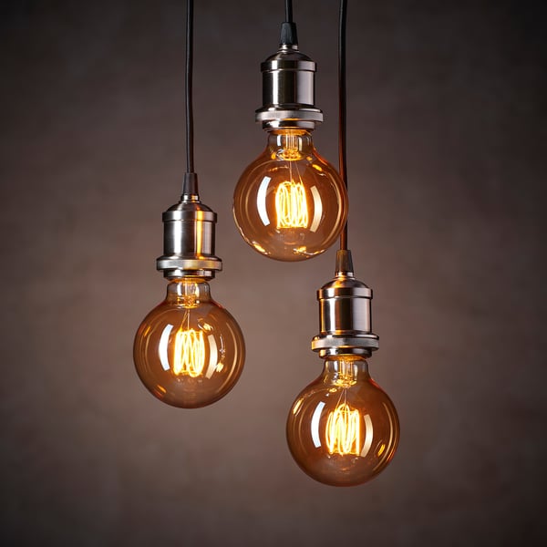 Trzy lampy wiszące w stylu vintage ze szklanymi żarówkami w kolorze bursztynu emitują ciepłe, przytulne światło.