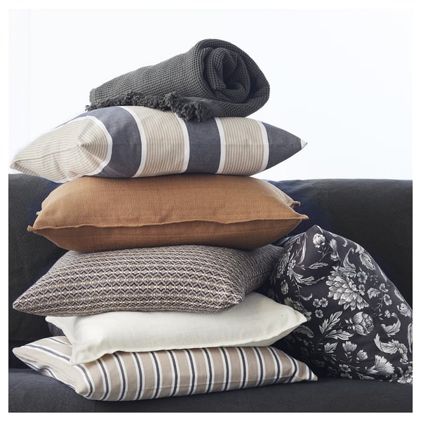 Stos szaro-beżowych poduszek, barwionych przędzą, w kształcie kwadratu z zamkiem błyskawicznym, wyeksponowanych na sofie.