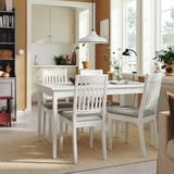 Biały kwadratowy stół jadalny z szarymi krzesłami, pionowe oparcia, przy dużych oknach.