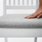 Dłoń osoby spoczywająca na miękkim, szarym, wyściełanym siedzisku nowoczesnego krzesła, podkreślająca wygodę i jakość tkaniny.