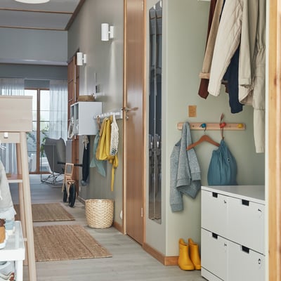 Zorganizowany korytarz z lampami NYMÅNE, wieszakiem na ubrania, żółtymi butami, rośliną i koszem.