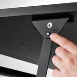 Ręka obsługuje czarną blokadę stolika kawowego, bezpiecznie regulując wysokość.